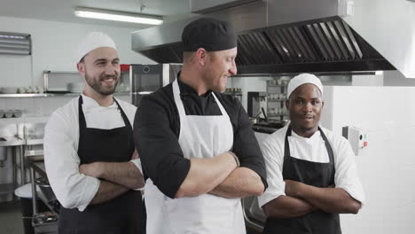 Group-of-happy-diverse-male-chefs-standing-with-arms-crossed-in-kitchen,-slow-motion