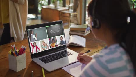 Schoolgirl-using-laptop-for-online-lesson-at-home,-with-diverse-teacher-and-class-on-screen