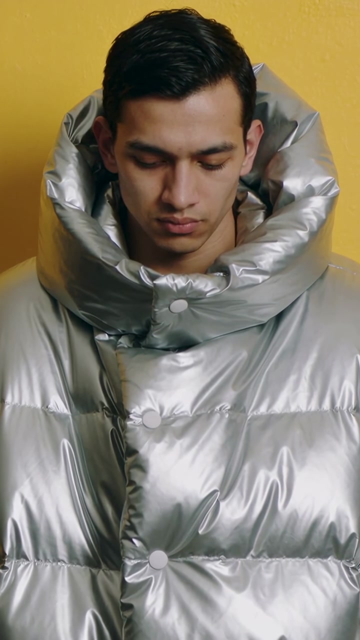 Vertical video: Camera starting, model holding down gaze in studio for shoot wearing silver coat