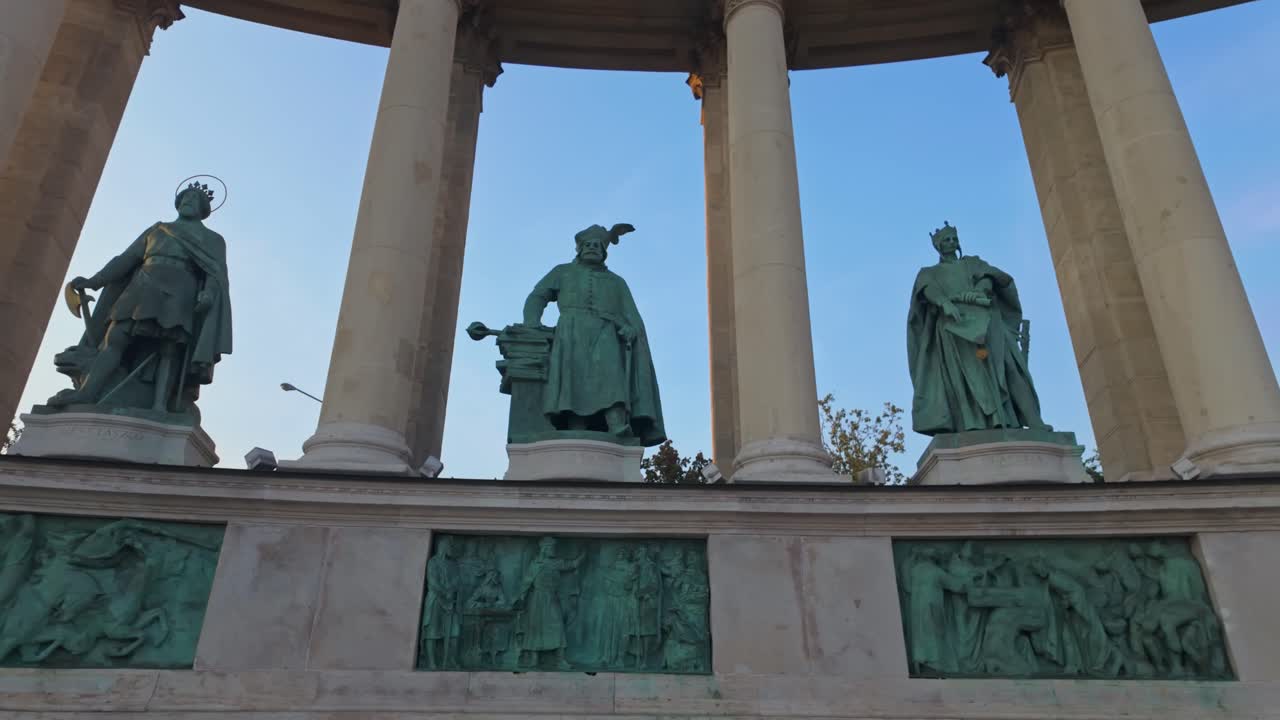 A cinematic pan right reveals statues of Hungarian leaders in the left colonnade of Heroes' Square, a historic and iconic UNESCO World Heritage site in Budapest, Hungary