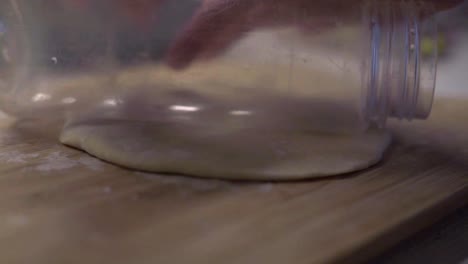 manos rodando masa con botella de plástico en tabla de cortar de madera, cerrar
