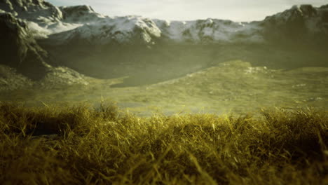 mountain landscape with snow capped peaks and golden grass at sunset