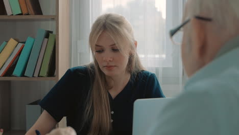 portrait of young caring nurse talking with elderly man in the office