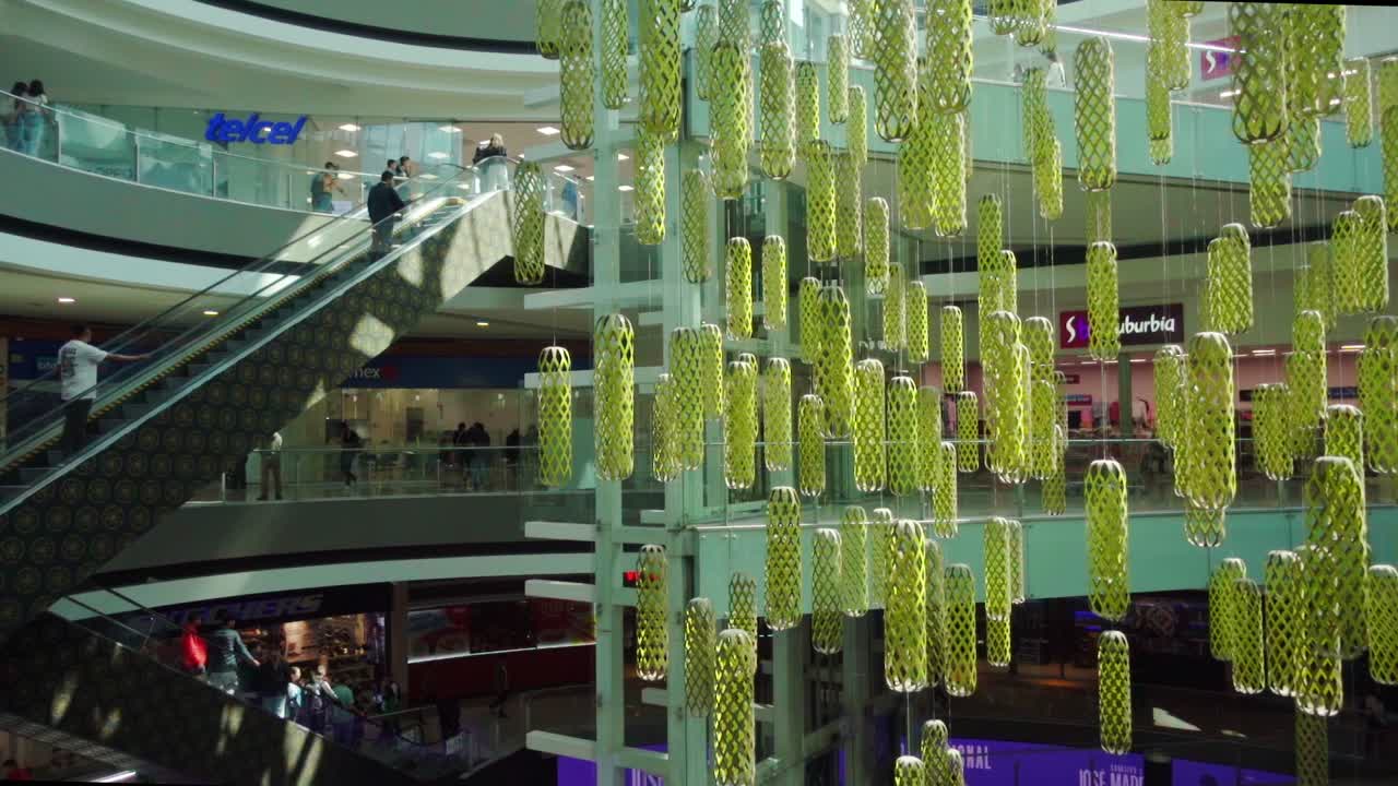 A modern shopping mall with colorful hanging decorations and people riding escalators indoors