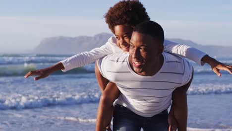 Afroamerikanischer-Vater,-Der-Seinem-Sohn-Am-Strand-Eine-Huckepackfahrt-Gibt