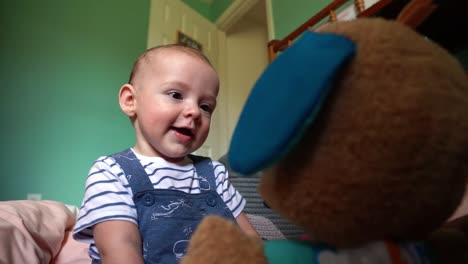 6-month-old infant boy laughing and smiling with stuffed animal in nursery