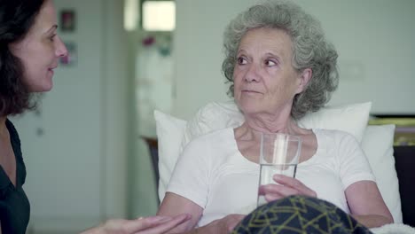 Beautiful-cheerful-nurse-giving-pills-to-elderly-woman-at-home.