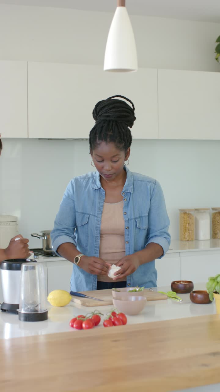 Video verticale: Amiche che iniziano la preparazione del pasto all'isola della cucina, una donna che rompe un uovo in una ciotola.