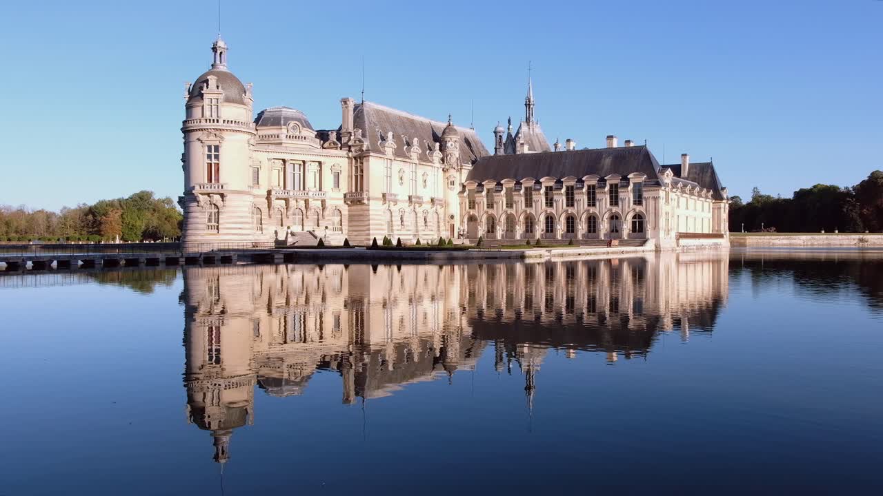 View of the Chateau de Chantilly castle surrounded by immense mirrors of water in Chantilly, Oise, France in daylight