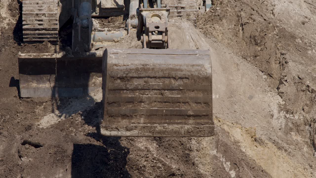 Excavator bucket lifts soil in daylight, overhead view, steady camera, earth-moving operation