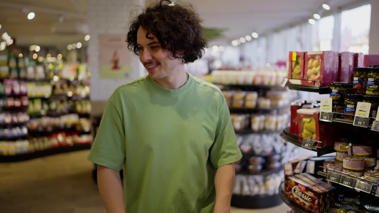 Happy brunette guy with curly hair and mustache walks and looks at goods in a grocery store while shopping