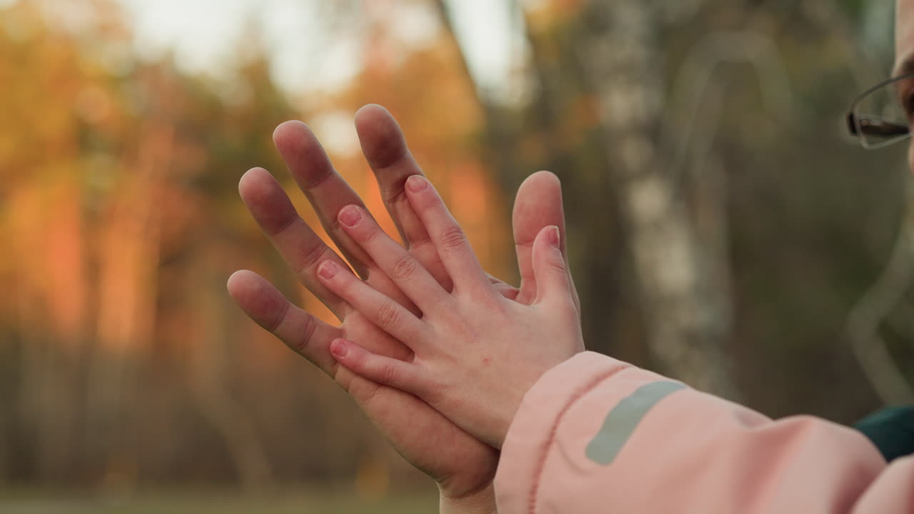 un momento tierno e íntimo capturado en un primer plano donde la mano de un niño se extiende para tocar la mano de una persona adulta, en un telón de fondo borroso de otoño con la cálida luz del sol