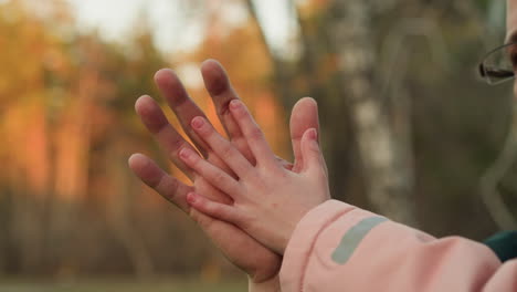 a tender and intimate moment captured in a close-up shot where a child's hand reaches out to touch an adult's hand, set against a blurred autumn backdrop with warm sunlight