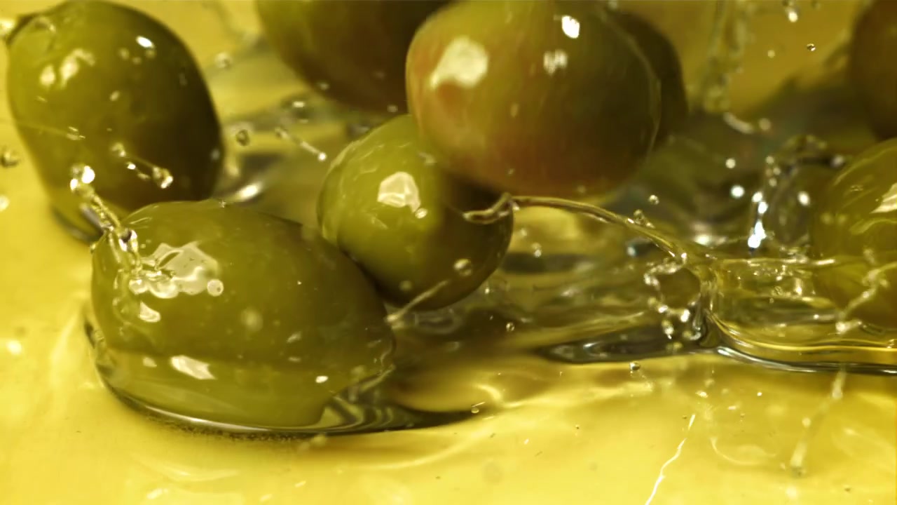Olive verdi che cadono e schizzano nell'olio d'oliva al rallentatore