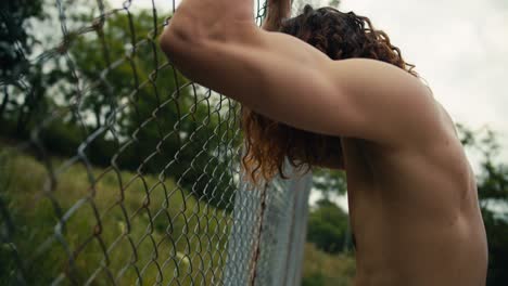 tired sad red-haired man beats his hands on the fence of the basketball court