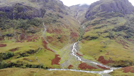 Luftaufnahme-Der-Dramatischen-Glencoe-Tallandschaft-In-Schottland-Mit-Fluss,-Der-Den-Berg-Hinunterfließt