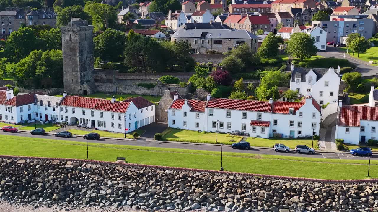 Drone pans across white houses, castle tower, and green landscape in bright daylight, Fife, Scotland