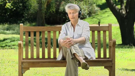 Aged-woman-listening-to-music-with-headset-on-a-bench