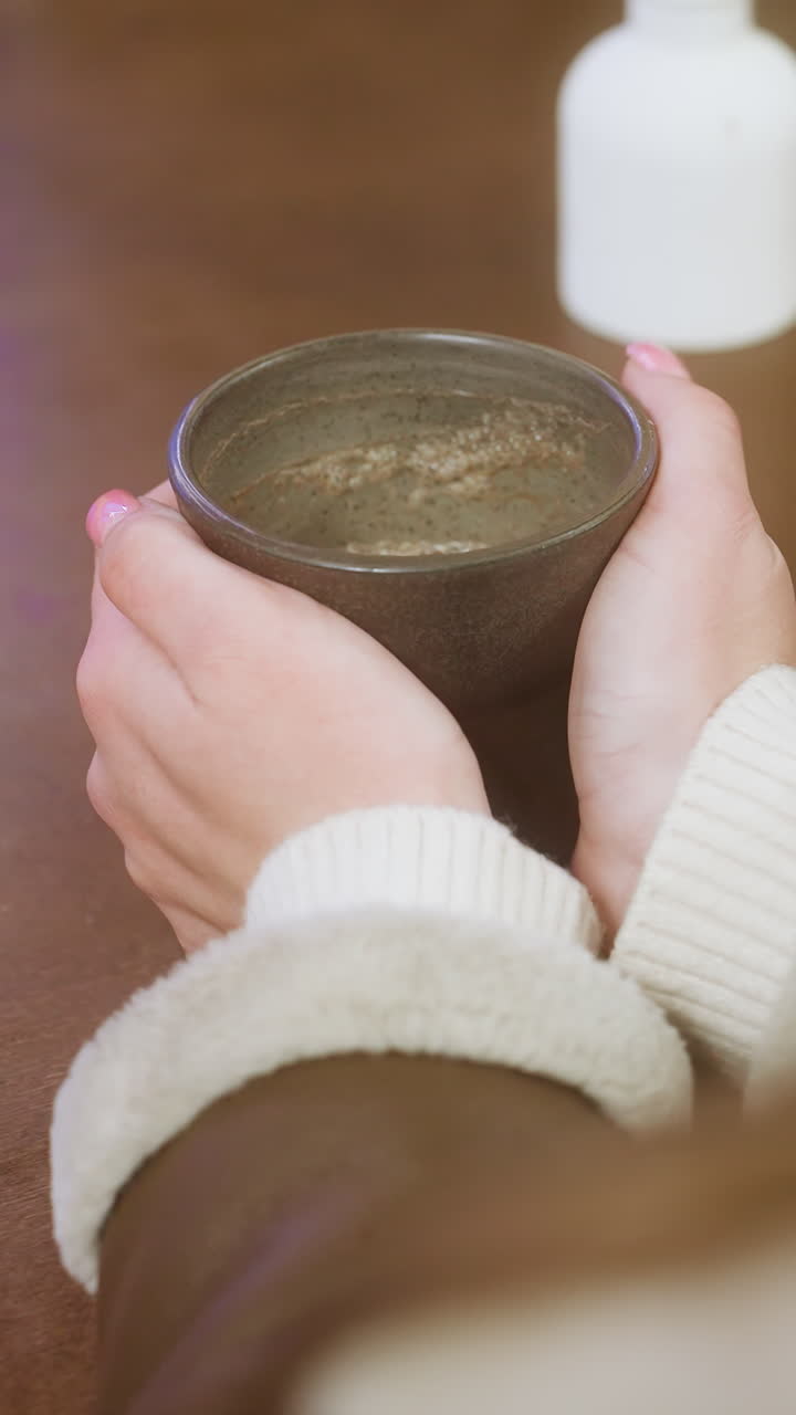 Close-up shot of woman's hand gently holding coffee cup on table, with soft lighting and cozy atmosphere, perfect for capturing moments of relaxation and enjoyment in a calm cafe setting
