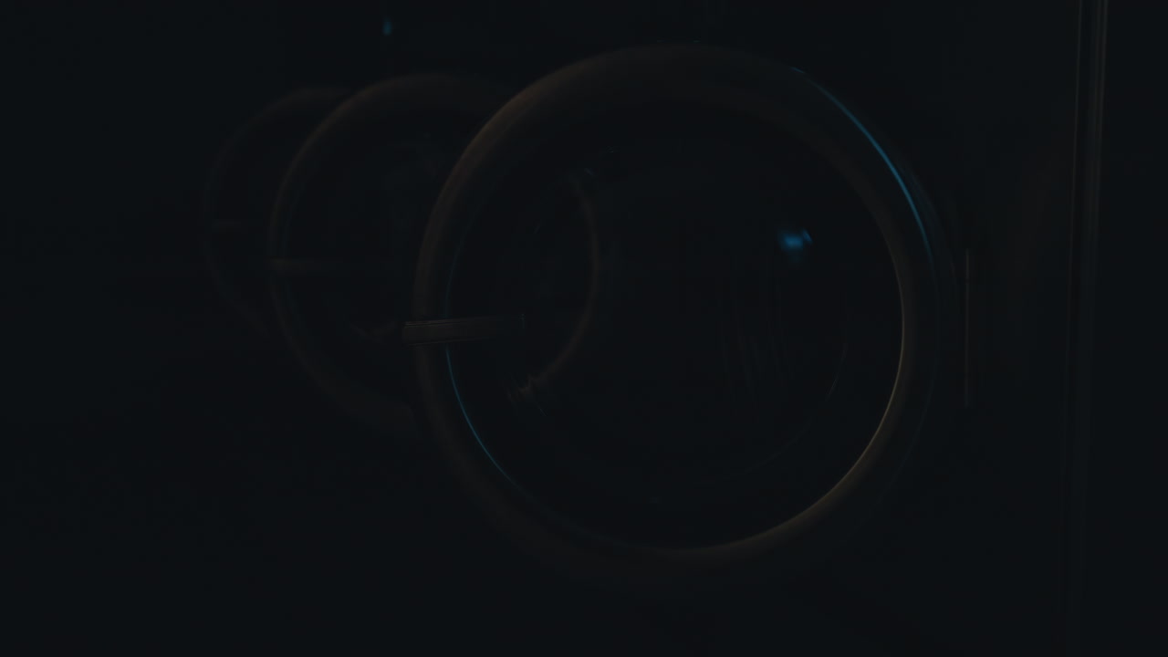 Row of industrial washing machines with metallic covers open in clean tiled laundry facility, illuminated by bright light before switching off, professional service environment