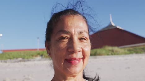 Mujer-De-Raza-Mixta-Mirando-A-La-Cámara-Y-Sonriendo-En-La-Playa-Y-El-Fondo-Del-Cielo-Azul