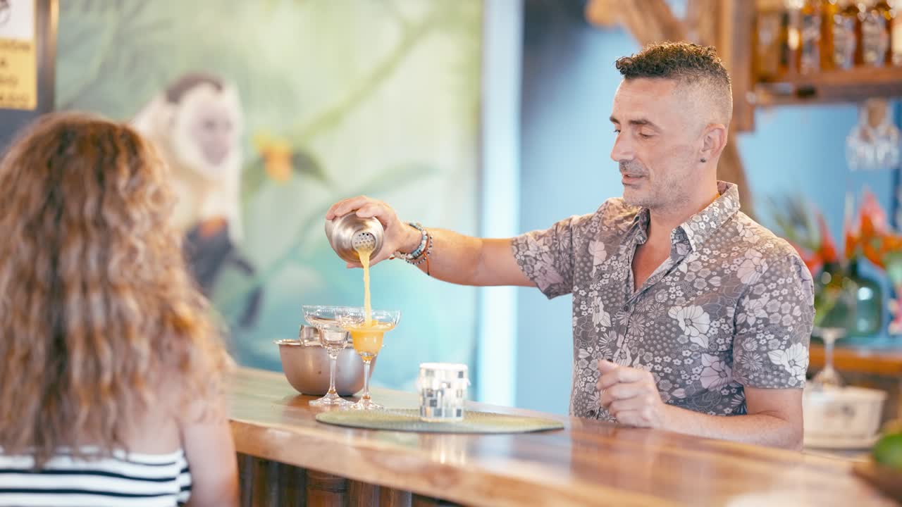 Barkeeper schenkt einem Kunden in einer tropischen Bar einen Cocktail ein.