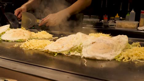 A-Japanese-chef-cooks-a-traditional-Okonomiyaki-savory-pancake-on-a-tepanyaki-grill-in-Kyoto,-Japan