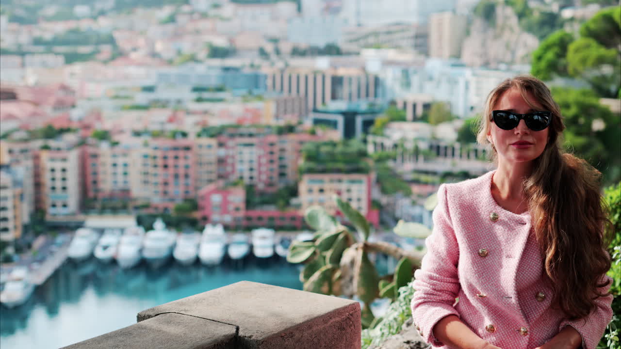 Brunette woman in a pink blazer smiling with a blurry view of boats docked in the Port de Fontvieille in Monaco
