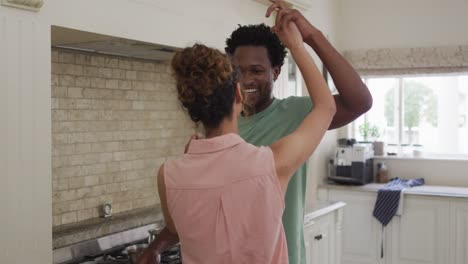 happy biracial couple dancing together in kitchen