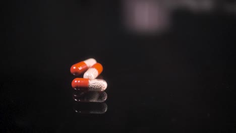 Pills-falling-down-on-a-black-glass-surface,-mirror-surface-with-a-reflection-on-black-background