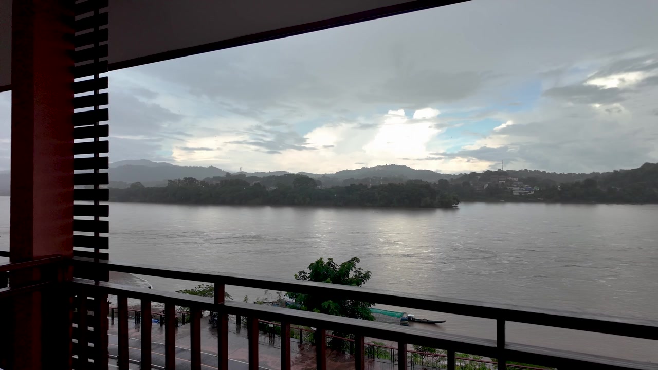 Vista da un balcone d'hotel che si affaccia sul fiume Mekong durante una giornata piovosa con il Laos sullo sfondo.