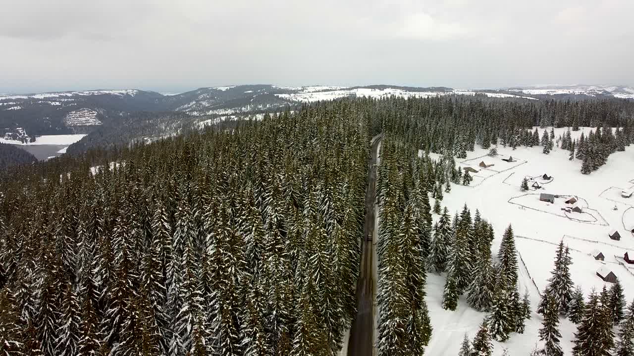 Droneutsikt over en bil som passerer gjennom den snødekte skogen.