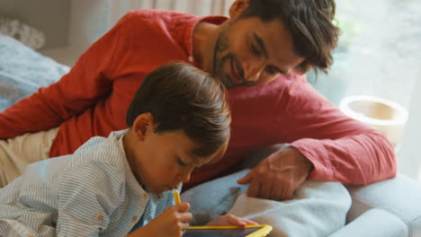 padre e hijo en casa en el sofá en la sala de estar jugando con el juego de dibujo juntos