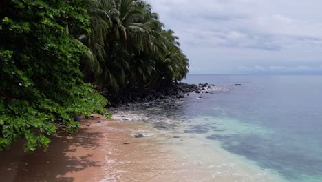 drone flyover turquoise colored water by tropical jungle of principe island