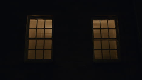 Moody-atmospheric-night-shot-of-two-windows-with-faint-orange-light-behind-on-dark-day