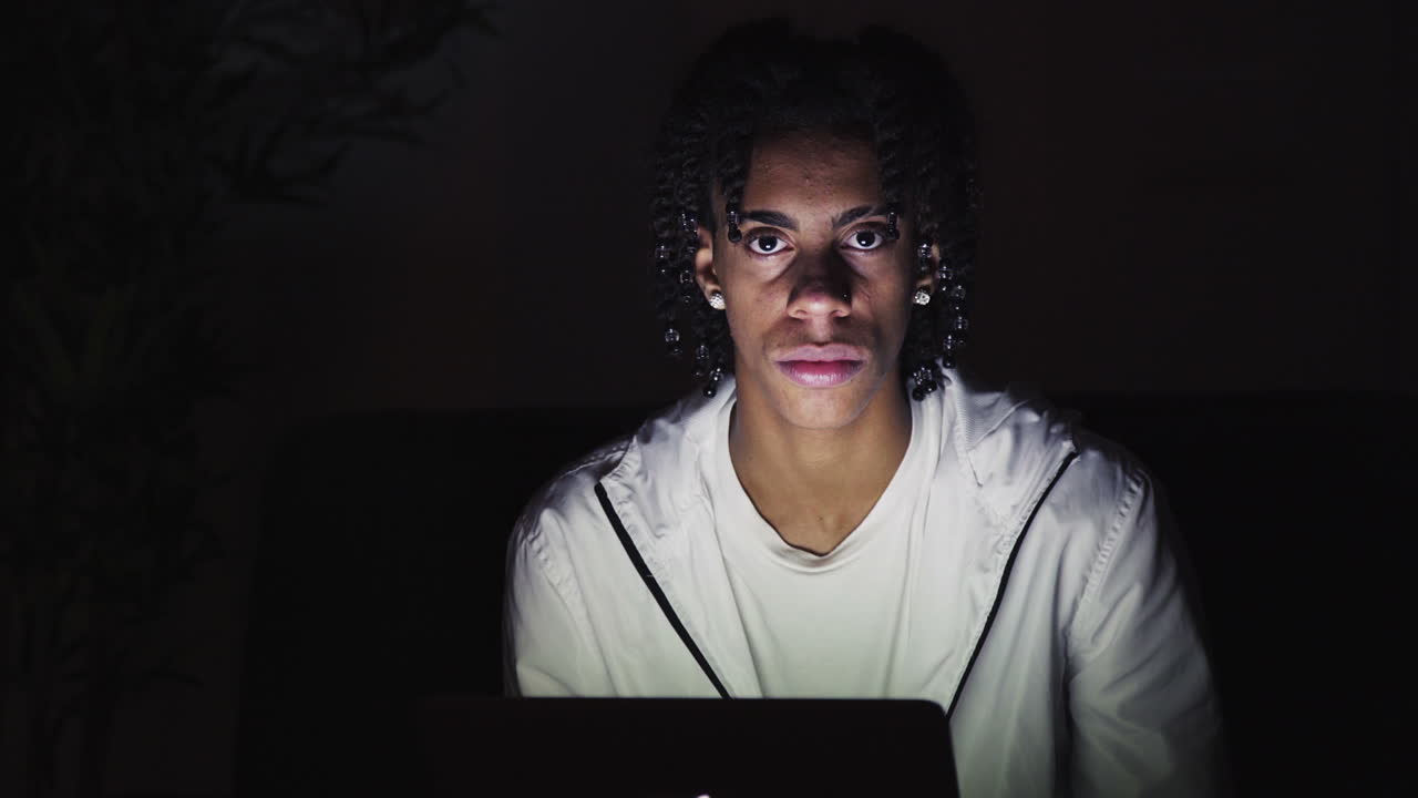 Portrait of serious young man sitting at laptop in dark room