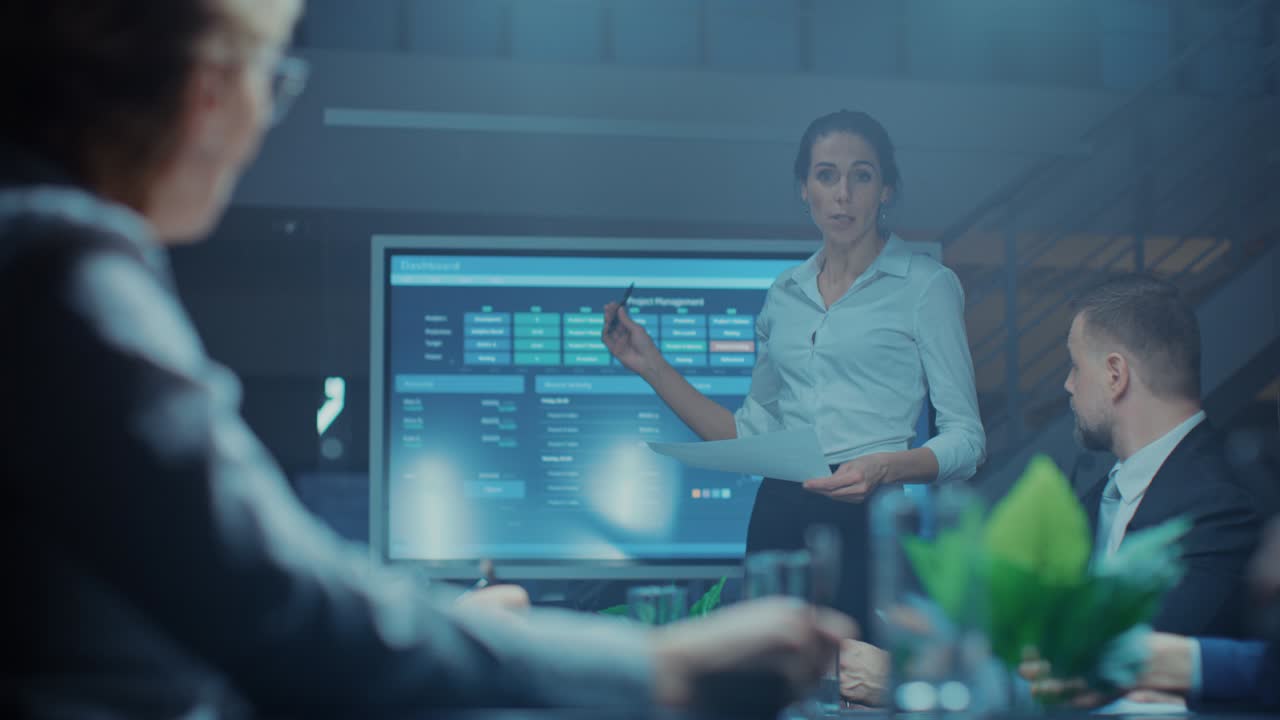 In the Corporate Meeting Room: Female Executive Makes a Speech and Uses Digital Interactive Whiteboard for Presentation to a Board of Directors, Investors. Screen Shows Growth Data. Late at Night Office