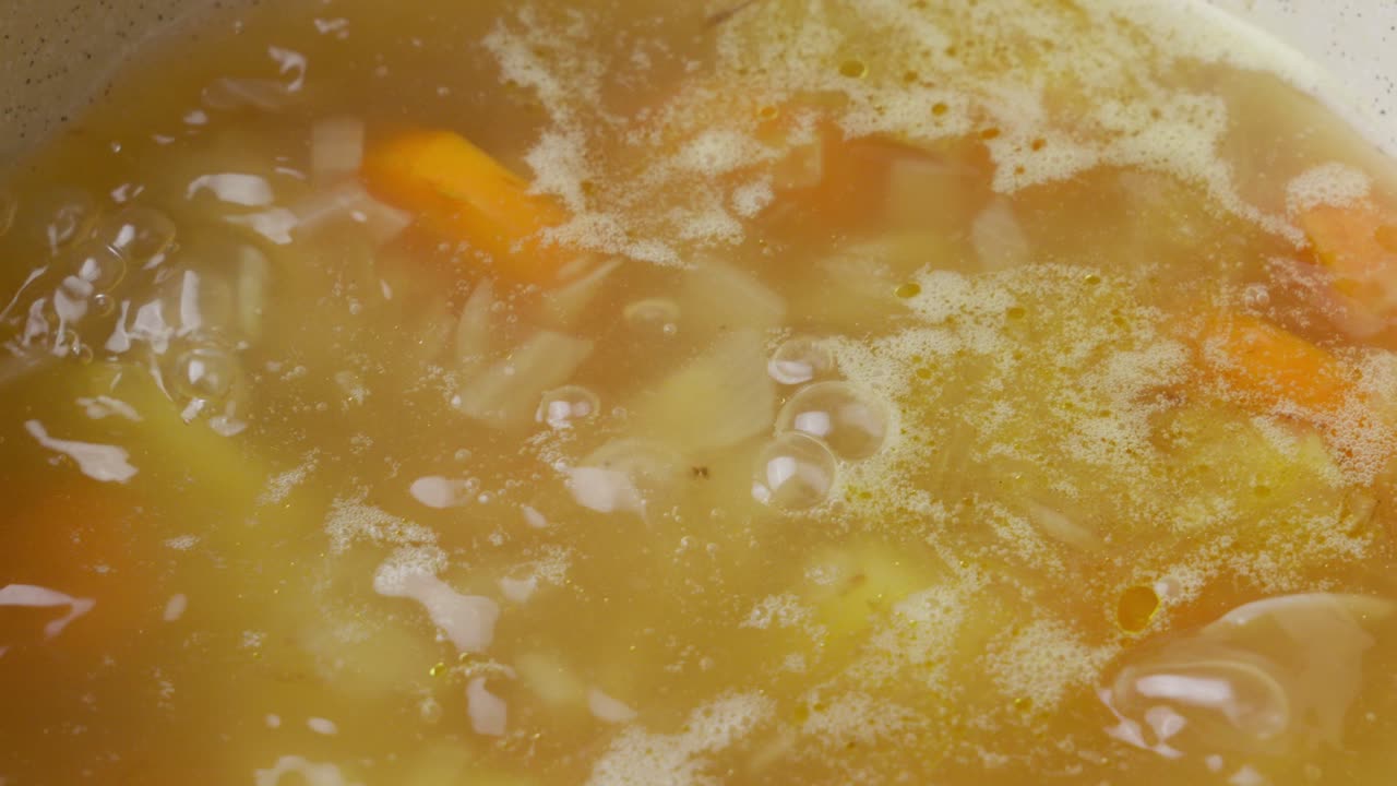 Zuppa con verdure e dado di pollo che sobbolle dolcemente.