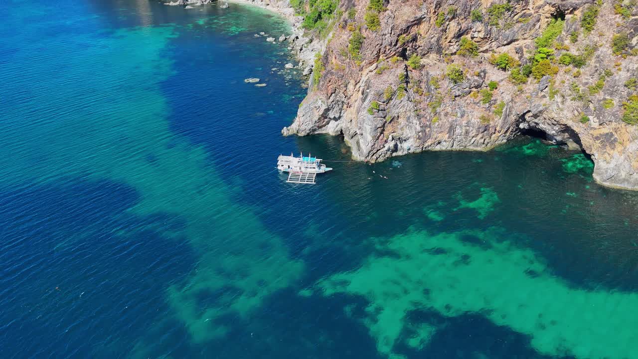 Drone footage of steep cliffs, turquoise water and a boat near Palawan in the Philippines