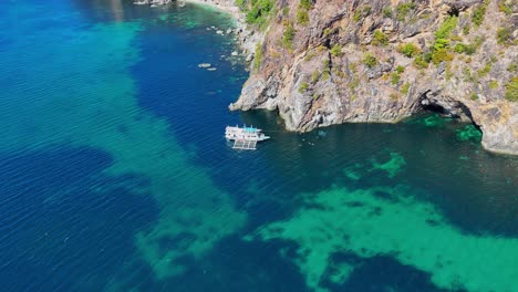 drone footage of steep cliffs, turquoise water and a boat near palawan in the philippines