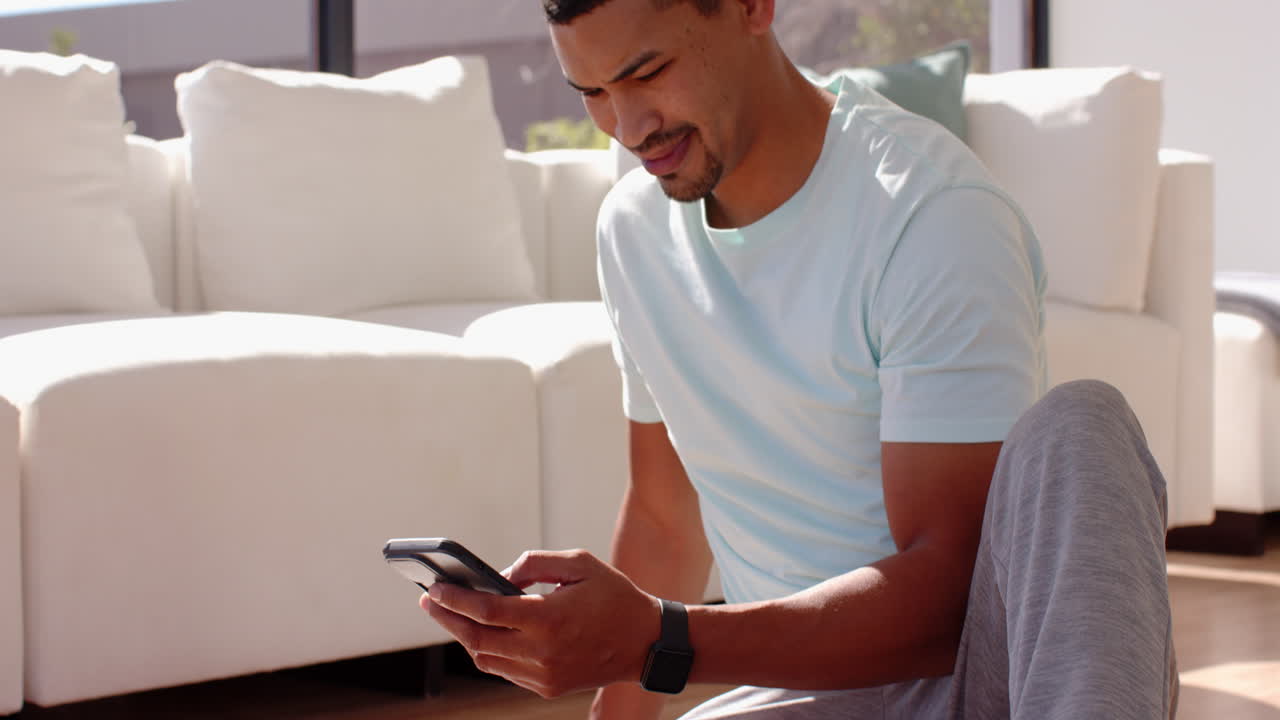 Using smartphone, man sitting on floor in living room, wearing smartwatch