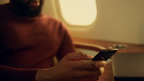 tipo usando teléfono móvil en primer plano en un avión privado. hombre barbudo sonriente sosteniendo las manos