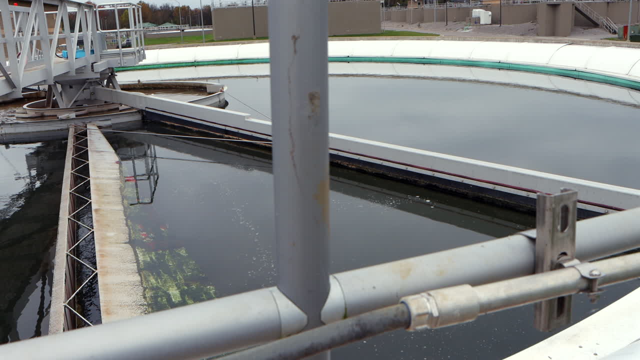 A clarifier pond at a wastewater treatment plant gently processes water, with suspended solids settling as the liquid flows, creating a dynamic industrial scene