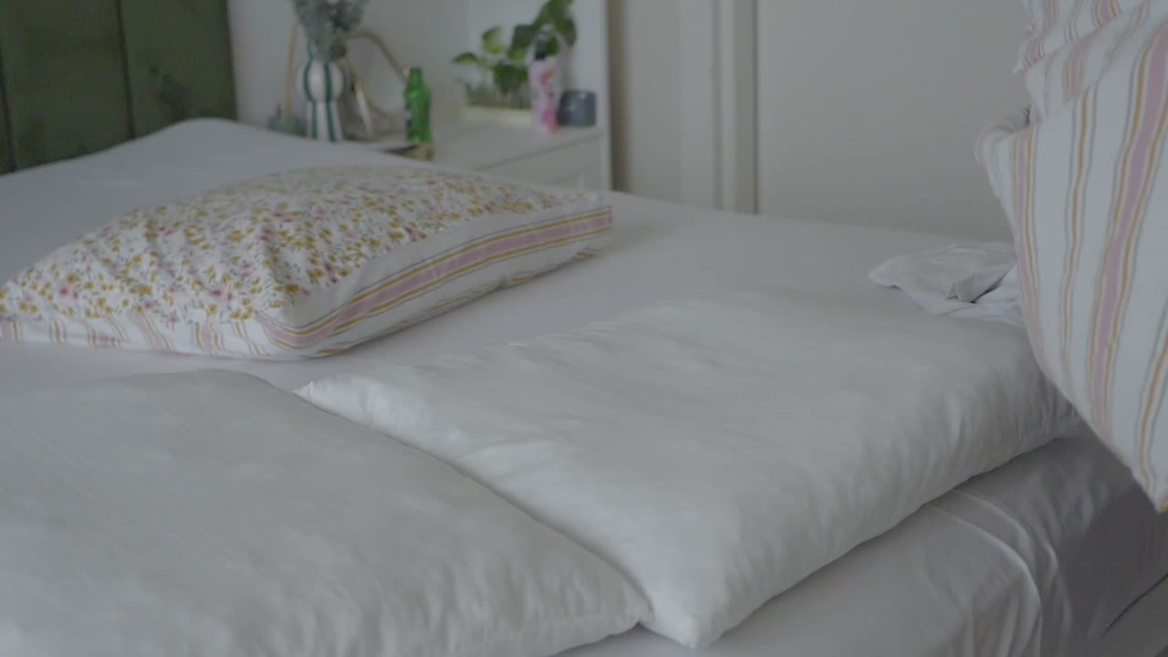 Person's Hands Removing a Striped Pillowcase from a Pillow on a Bed