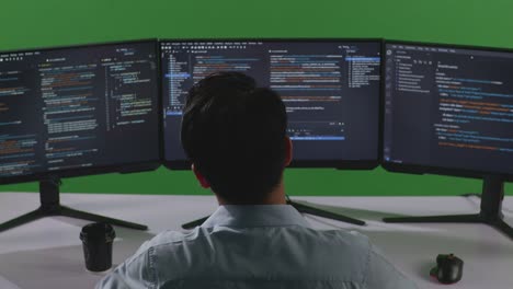 back view of tired asian man developer stretching while write code with multiple computer screens in green screen studio