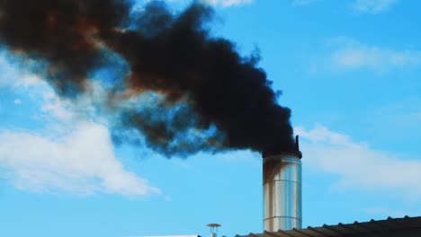 humo negro espeso saliendo de la chimenea de fábrica, fondo de cielo azul