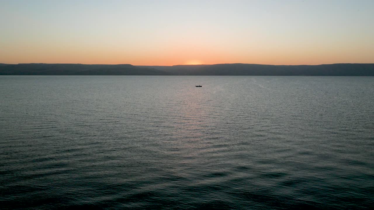 vista aérea de drones, movimiento lento: volando sobre el mar al amanecer o al atardecer, con un barco solitario en el fondo, una línea de horizonte naranja y olas tranquilas creando un patrón relajante