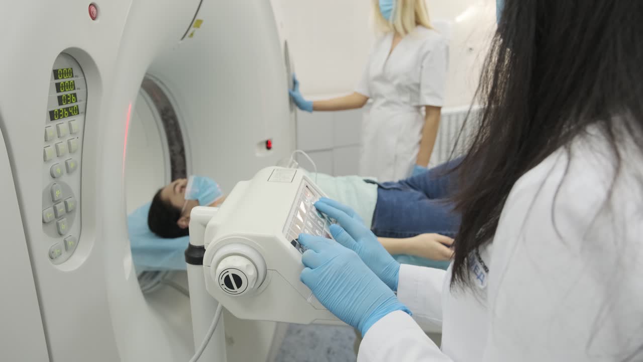 Female patient is undergoing CT or MRI scan under supervision of two qualified radiologists in modern medical clinic. Patient lying on a CT or MRI scan table, moving outside the machine