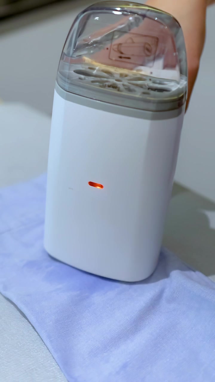 Primo piano di una mano che usa un levapelucchi elettrico bianco su un tessuto di indumento blu all'interno.