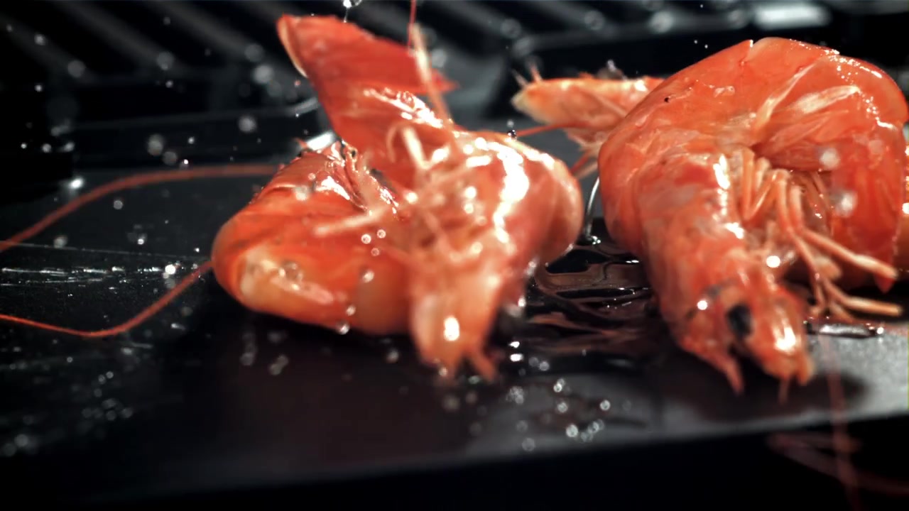 Gamberi che sfrigolano su una griglia calda con schizzi d'olio in slow motion